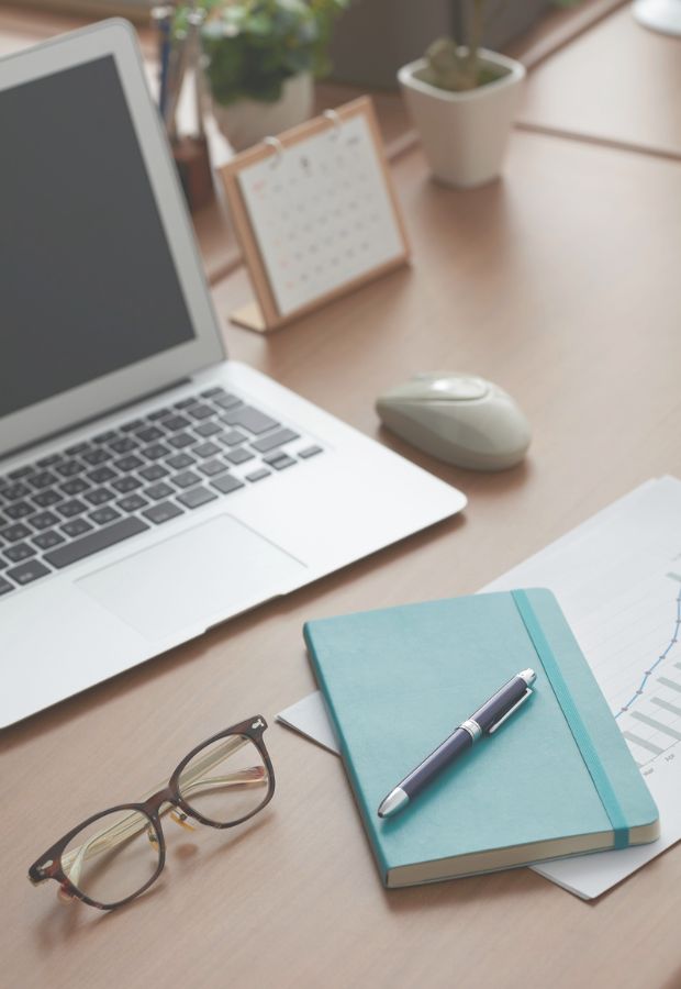 Imagen de fondo de un escritorio con una computadora, gafas y elementos de libreria